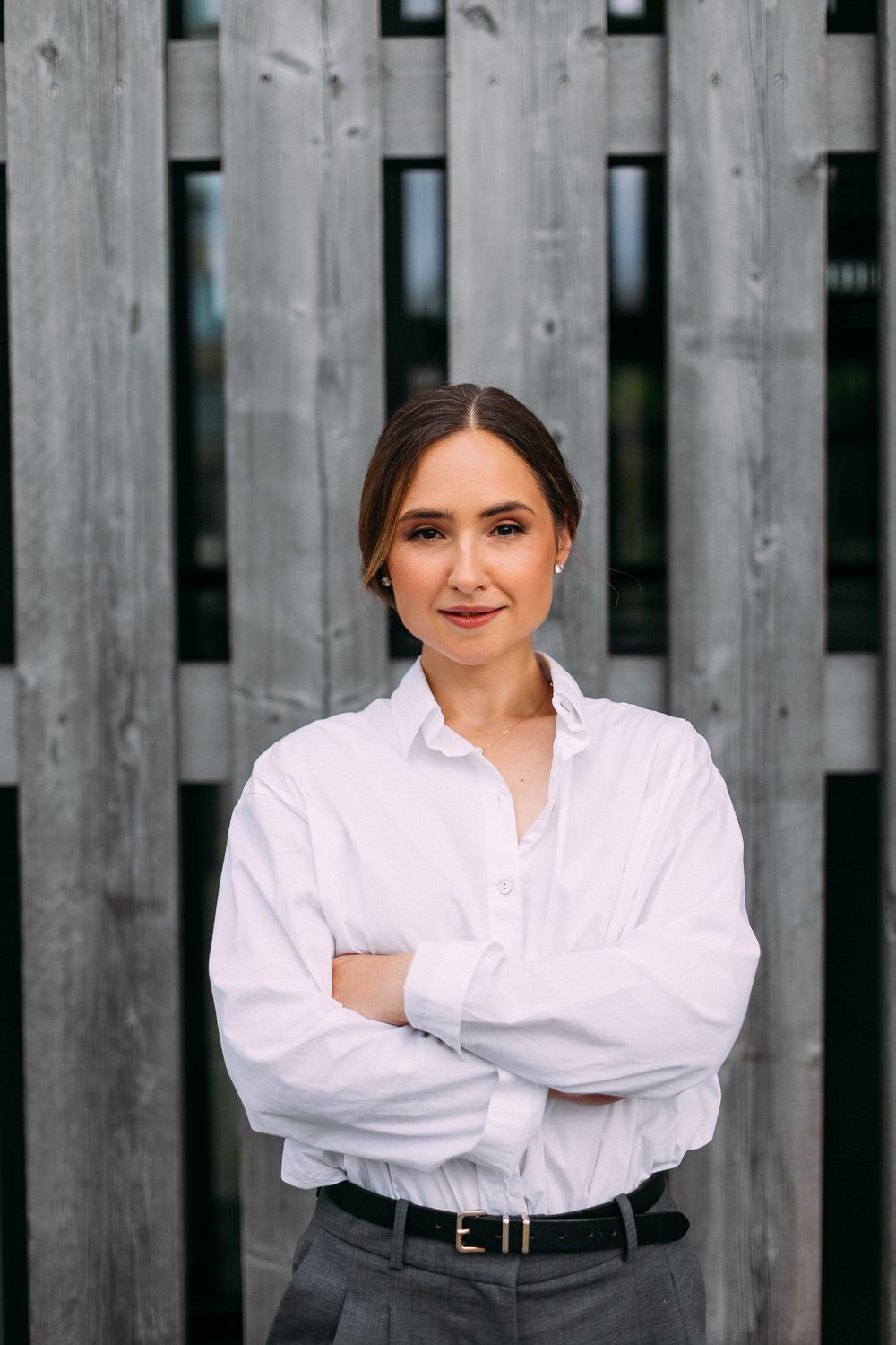 Viktorija Garanca, arms crossed, in a white shirt in front of a grey timber wall